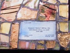 Picture of glass mosaic on wood gold glass with text of business card under glass that says: Vulcan Scrap Metal Co. Non-Ferrous Metals and Scrap Junk Cars  105 Worth Street Stamford, Conn Fireside 8-4339 Carmine Longo / Art Rossi