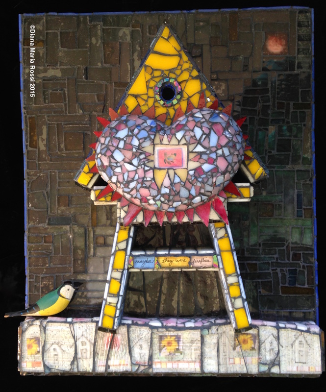 photo of glass mosaic heart on a house-shaped structure, kind of like a tree-house. The heart is pink and light blue with a photo of a nest mosaic in the center. This next mosaic photo is small and offset by yellow spokes. The tree structure is yellow and blue and it sits on a strip of 