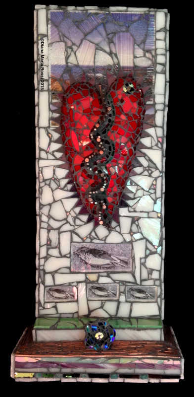photo of glass mosaic heart. the heart is red with a zigzag stripe down the middle with nails in it. It is on a white glass background,but the upper portion has a photo under transparent glass. It is a very purple photo of the coast of Maine. On the bottom there is an altar like protrusion with a flower like vase turned on its side facing the audience. the vase is made from dichroic glass so looks rainbow like with an emphasis on colors in the blue/indigo spectrum!!!