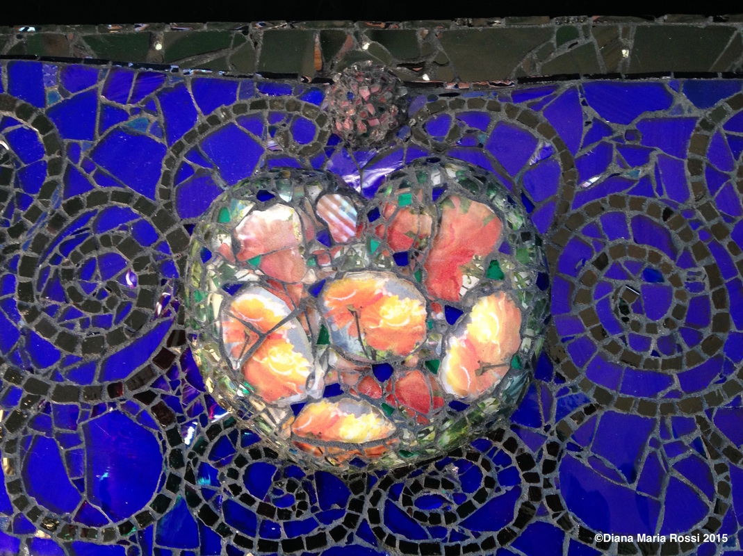 detail of photo of glass mosaic heart. heart is transparent glass over photos of roses and the roses are orange and yellow. the background is cobalt blue with black swirls