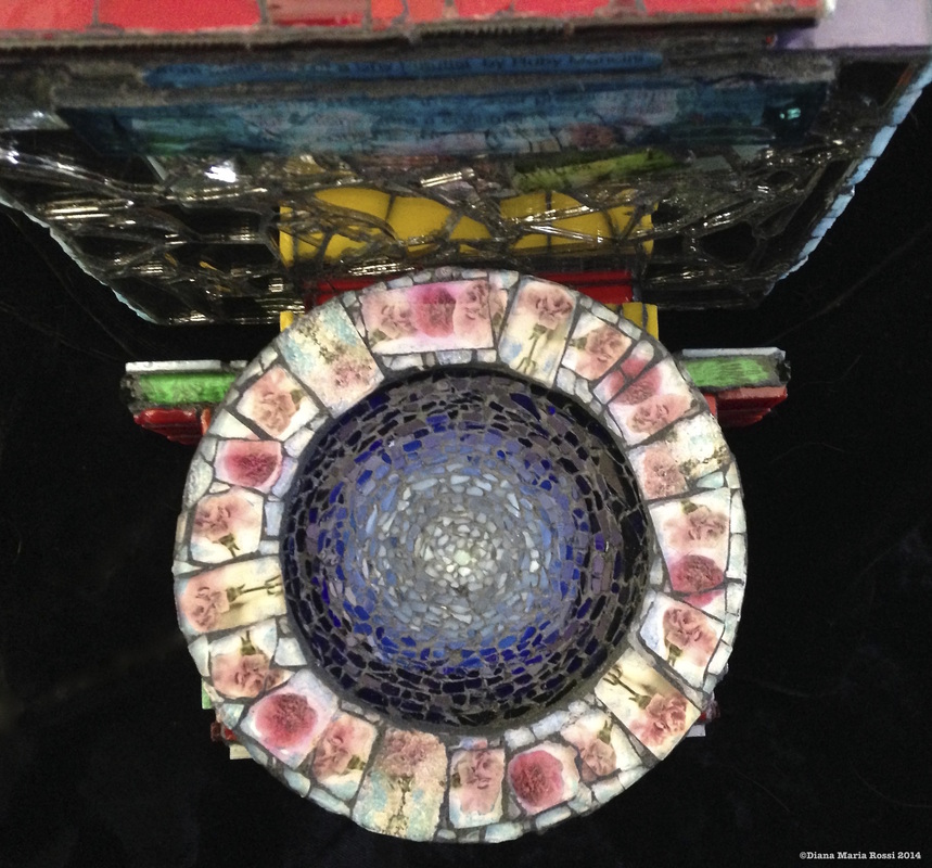 Picture of glass mosaic on wood detail blue roundel surrounded by pink carnations under glass in a wreath shape