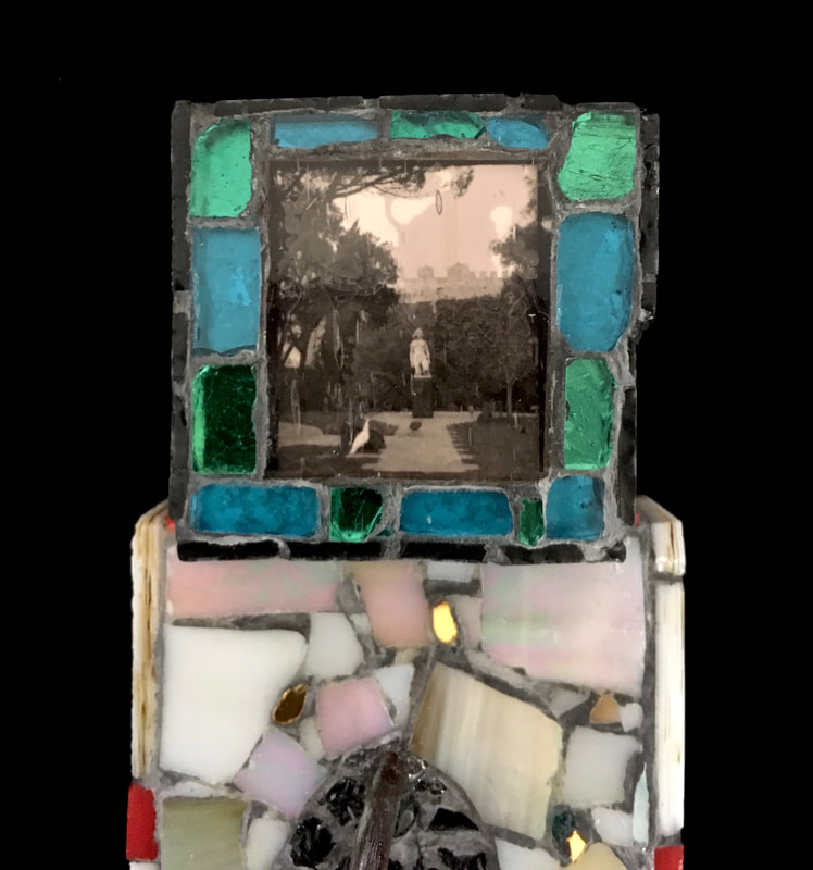 detail of Eve's Place Redux - the top tv head part -- a cube with a photo of a park in either Spain or Portugal of a woman's statue. The photo is in black and white with a pink cast and is surrounded by green and aqua colored glass